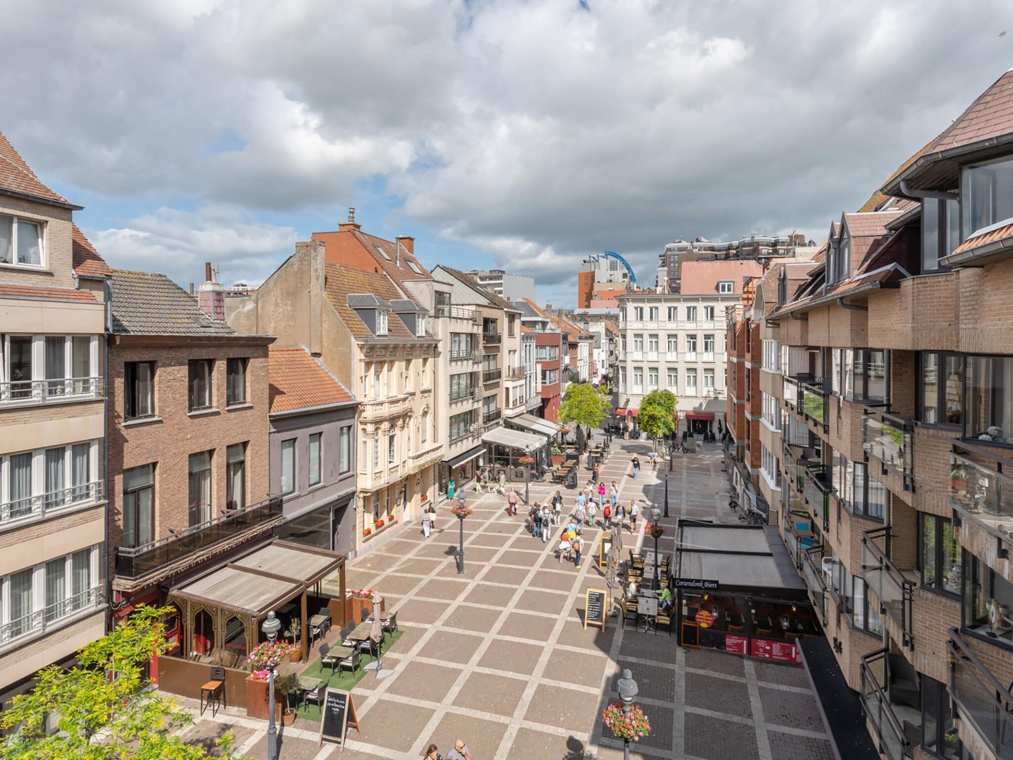 Une place carrée bordée de cafés et de boutiques, entourée de bâtiments historiques à l’architecture variée.