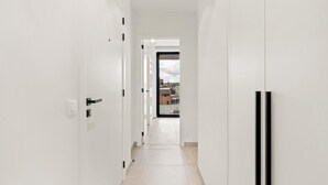A narrow, white-walled hallway with a tiled floor leading to a door with a view of buildings outside. - Beautiful apartment in the center (Blankenberge)