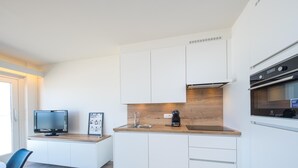 Eine moderne Küche mit weißen Schränken, einer Holzarbeitsplatte, einem eingebauten Ofen und einem Fernseher auf einem Standfuß.