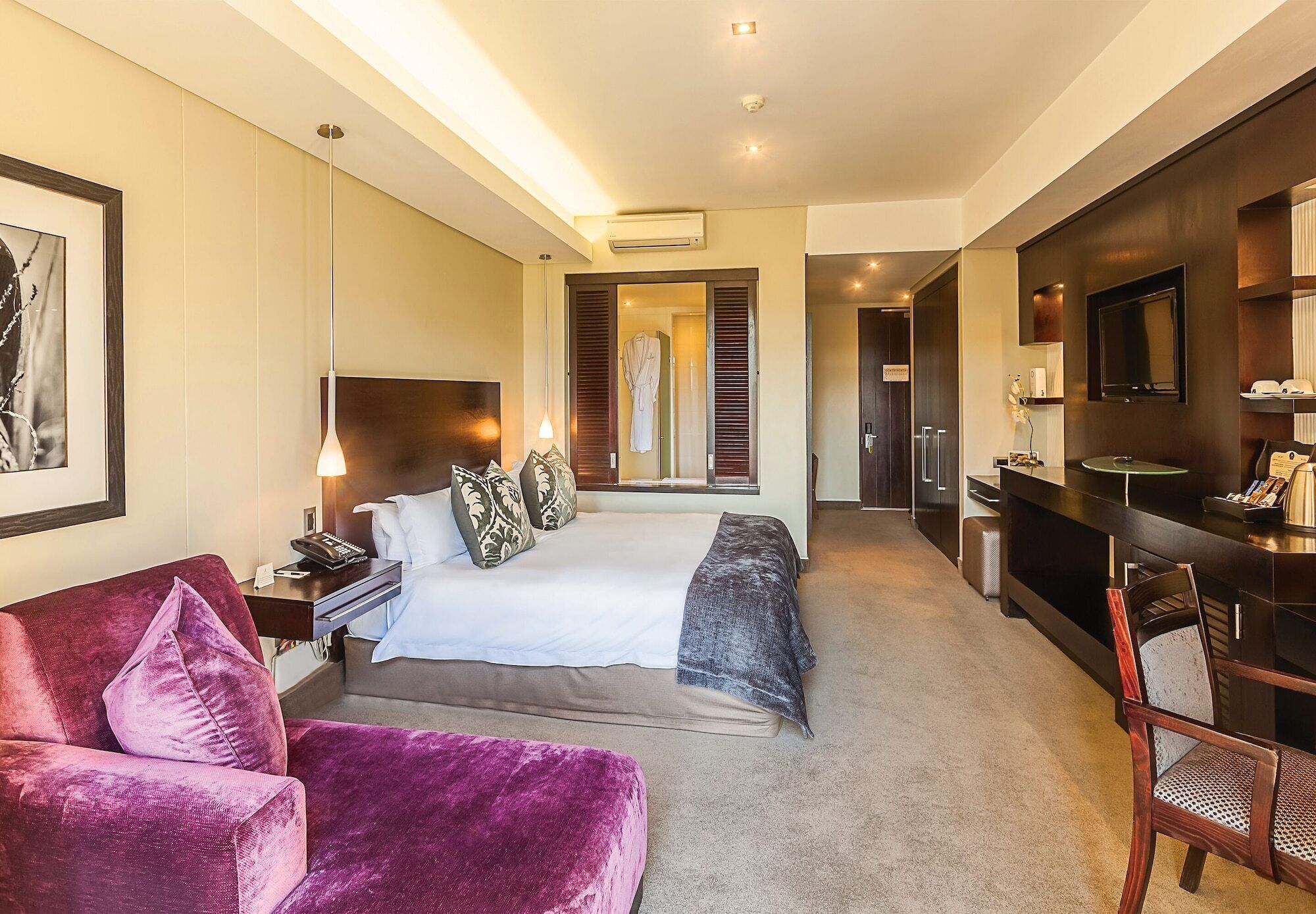 A modern hotel room with a large bed, a desk, a TV, and a bathroom visible through an open door.