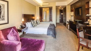 Habitación de hotel moderna con una cama grande, un escritorio, un televisor y un baño visible a través de una puerta abierta.