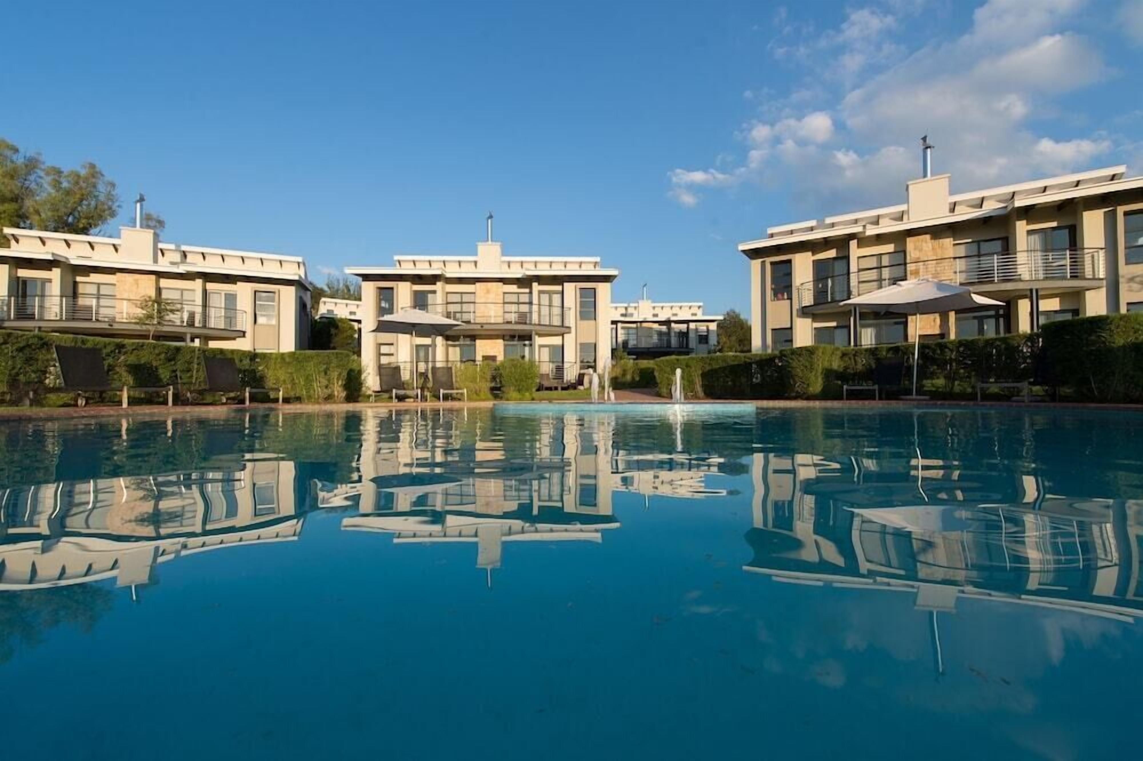 Un hôtel moderne doté d’une piscine, dont l’architecture se reflète dans l’eau et dans le ciel.