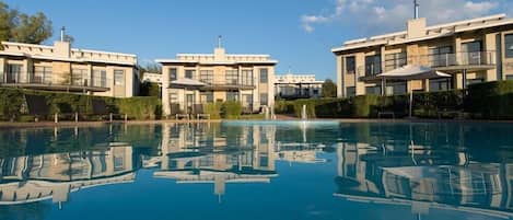 A modern hotel with a swimming pool, reflecting the buildings and sky.
