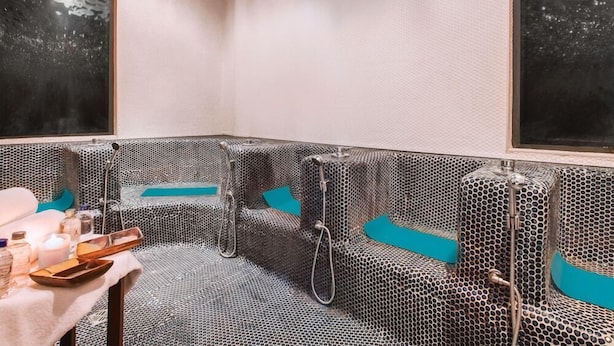 Un cuarto de spa con una zona de estar con diseño, una camilla de masaje y una mesita con velas y botellas.