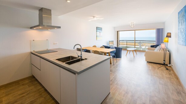 A modern kitchen with a central island, a dining area with a view, and a living space with a balcony. - Modern apartment with direct sea view (Middelkerke)