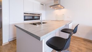A modern kitchen with a central island, built-in ovens, and a stainless steel range hood. - Modern apartment with direct sea view (Middelkerke)