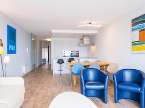 A modern living room with a sofa, a dining table with chairs, and a kitchen in the background. - Modern apartment with direct sea view (Middelkerke)