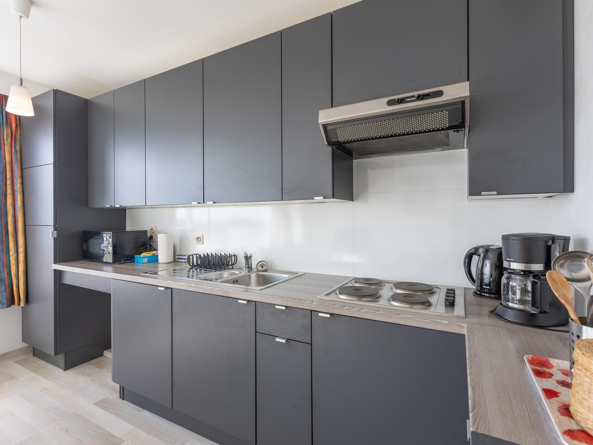Een moderne keuken met grijze kastjes, een roestvrijstalen spoelbak en een inbouw afzuigkap.