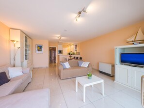 A modern living room with a sofa, a coffee table, and a TV. There is a kitchen in the background with a dining area. - Apartment on the 5th floor with sea view (Middelkerke)