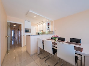 A modern kitchen with a built-in oven and microwave, a dining area with a table and chairs, and a hallway leading to another room. - Apartment on the 5th floor with sea view (Middelkerke)