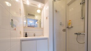 Ein modernes Badezimmer mit Duschkabine aus Glas, einem weißen Waschbecken mit Spiegel darüber und einem kleinen Ablagebereich für Toilettenartikel.