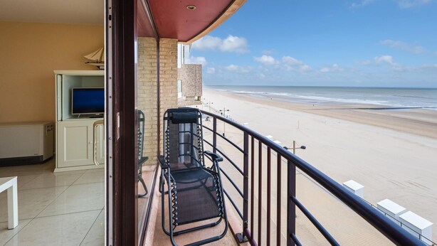Ein Balkon mit Blick auf den Strand, einem Fernseher und einer Sitzecke.