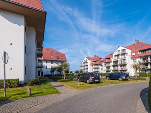 A residential building with a red roof, multiple balconies, and a paved driveway with parked cars. - Cozy apartment with terrace (Middelkerke)