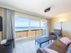 Una habitación de hotel con balcón, un sofá, una mesita de café, un televisor y una lámpara.