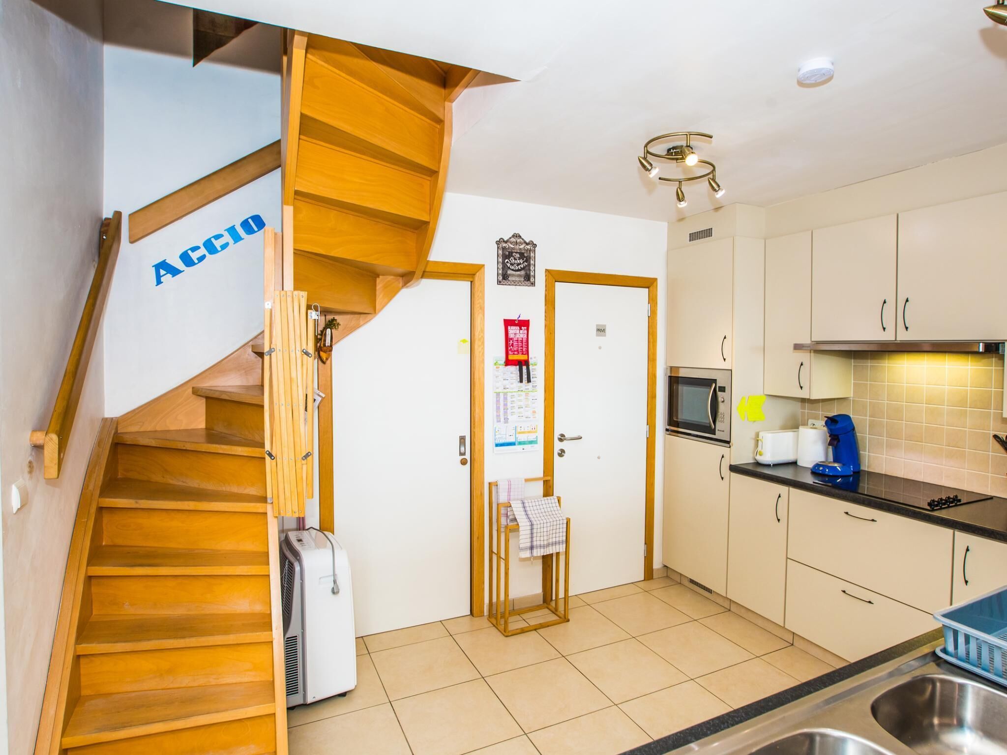 A kitchen with a wooden staircase, a microwave, a coffee maker, and a sink.