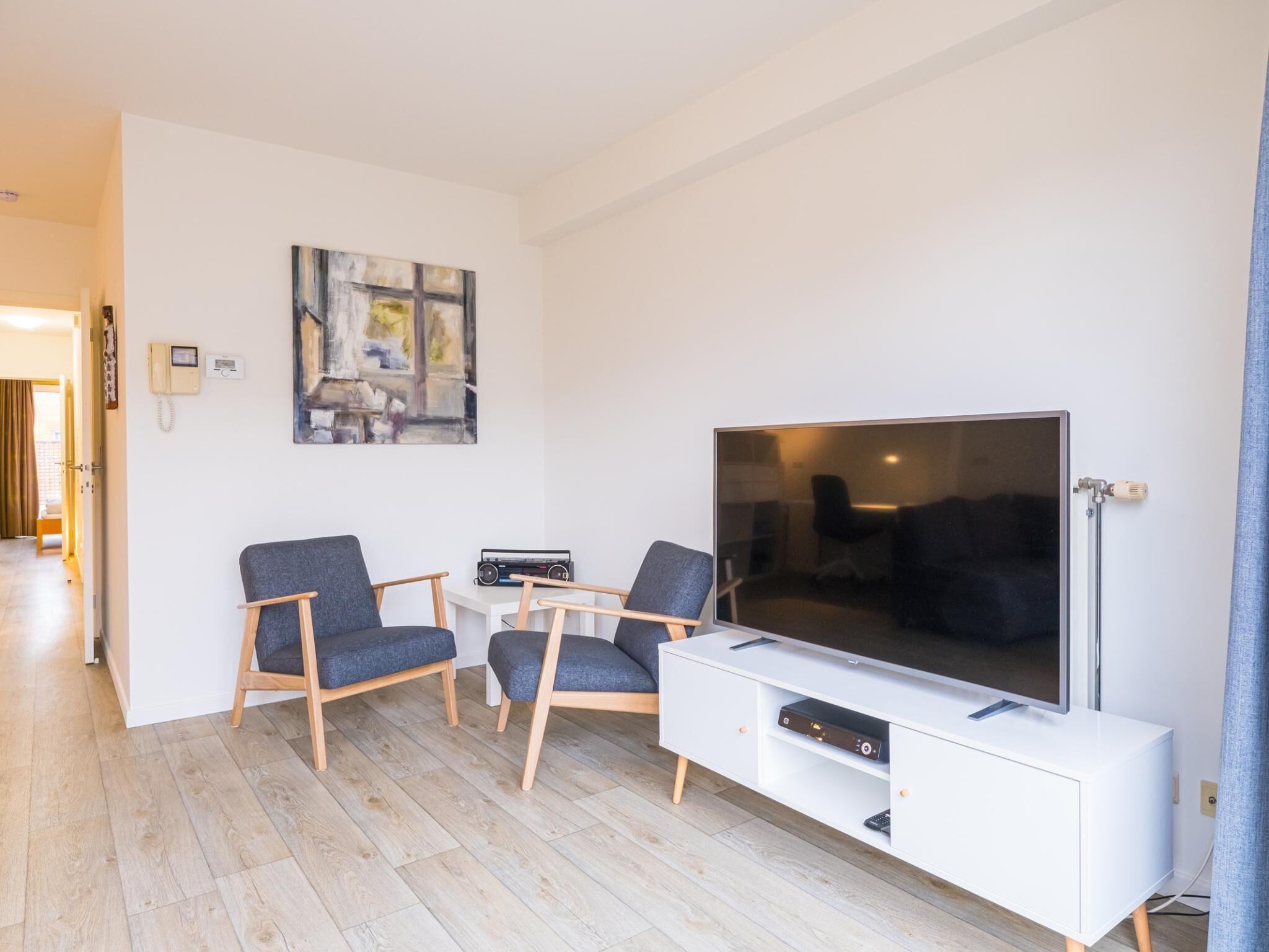 Ein modernes Wohnzimmer mit Flachbildfernseher, zwei Sesseln, einem Couchtisch und einem Gemälde an der Wand.