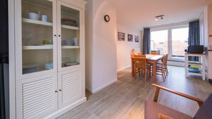 Una sala de estar moderna con comedor, piso de madera y un mueble blanco grande con puertas de vidrio.