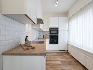 A modern kitchen with white cabinetry, a wooden countertop, a built-in oven, and a window with sheer curtains. - Corner apartment with phenomenal sea view (Middelkerke)