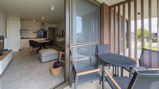 En moderne stue med en glasdør, der fører til en balkon, et spiseområde og et køkken.