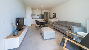 En moderne stue med en grå sofa, et spisebord med stole, og et køkken i baggrunden.