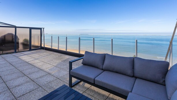 A balcony with a sofa and a glass enclosure overlooking a beach. - Exclusive penthouse with breathtaking 360° view (Middelkerke)