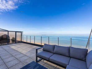 A balcony with a sofa and a glass enclosure overlooking a beach. - Exclusive penthouse with breathtaking 360° view (Middelkerke)