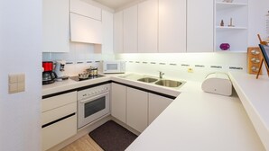 Una cocina compacta con gabinetes blancos, microondas, cafetera y lavamanos.