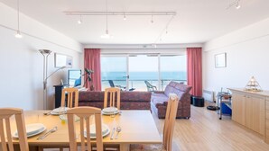 Un comedor moderno con una mesa lista para cuatro personas, un sofá y vistas al océano.