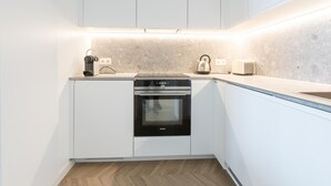 Une cuisine moderne avec des meubles blancs, un four encastré, une bouilloire et un grille-pain.