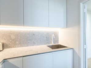 A modern kitchen with a granite countertop, stainless steel sink, and white cabinetry. - Bright apartment with direct sea view (Middelkerke)