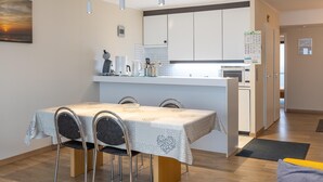 A modern kitchen with white cabinets, a dining table with chairs, and pendant lights. - Charming apartment near the beach (Middelkerke)