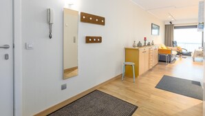 A modern hotel room with a wooden floor, a small stool, a desk with a chair, a bed, a large mirror, wall-mounted light fixtures, and a door with a key lock. - Charming apartment near the beach (Middelkerke)