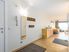 Ein modernes Hotelzimmer mit Holzboden, einem kleinen Hocker, einem Schreibtisch mit Stuhl, einem Bett, einem großen Spiegel, Wandleuchten und einer Tür mit Schlüsselsperre.