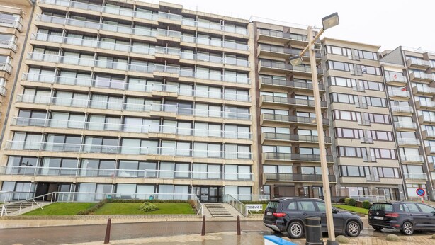 A multi-story residential building with a uniform facade, balconies, and a paved entrance area with steps leading to the entrance. - Charming apartment near the beach (Middelkerke)