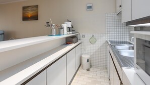 A modern kitchen with white cabinets, a stainless steel sink, and a coffee machine. - Charming apartment near the beach (Middelkerke)
