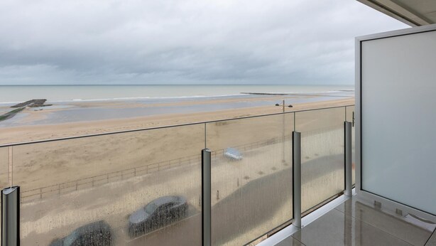 Varanda com vista para uma praia e oceano sob céu nublado.