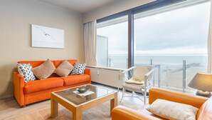 Uma sala de estar moderna com uma janela ampla, um sofá, uma poltrona e uma mesa de centro.