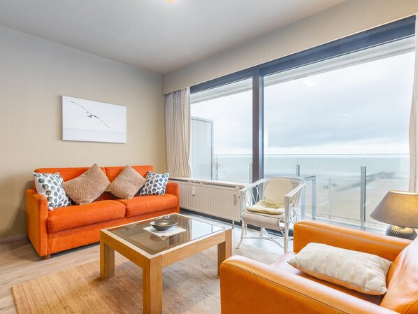 Ein modernes Wohnzimmer mit großem Fenster, einer Couch, einem Sessel und einem Couchtisch.