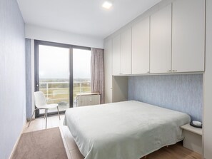 Ein modernes Schlafzimmer mit einem großen Bett, einem Sessel, einem Heizkörper und Blick durch ein großes Fenster.