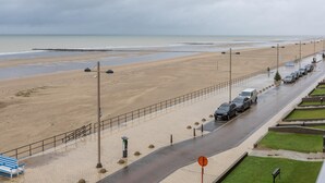 Uma estrada costeira com uma praia de um lado e um estacionamento com carros do outro.