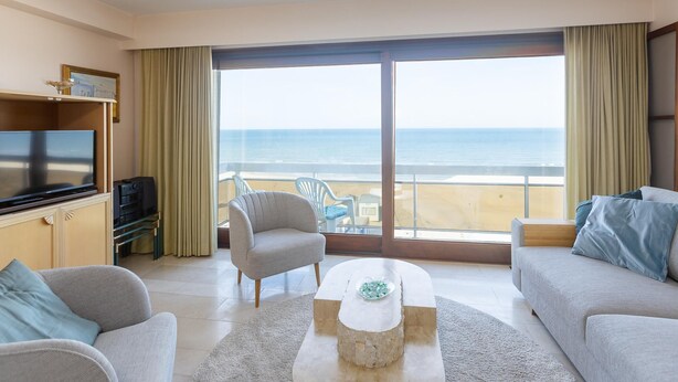 Una sala de estar moderna con un amplio ventanal que ofrece vista a la playa.