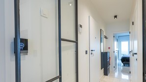 En modern hotellkorridor med en digital termostat, en glasvägg och utsikt över ett sovrum.