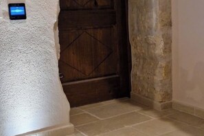 A textured white wall with a small device mounted on it, a wooden door with a diamond pattern, and a stone wall adjacent to the door. - My Sardinia - Il Lentisco: Sardinian Elegance and Charm in the Heart of Codrongianos (Codrongianos)