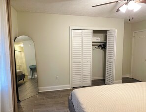 A bedroom with a bed, a closet with sliding doors, a mirror, and a ceiling fan.