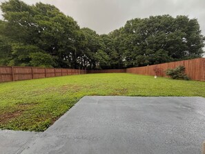 A backyard with a wooden fence, a concrete patio, and a grassy lawn.