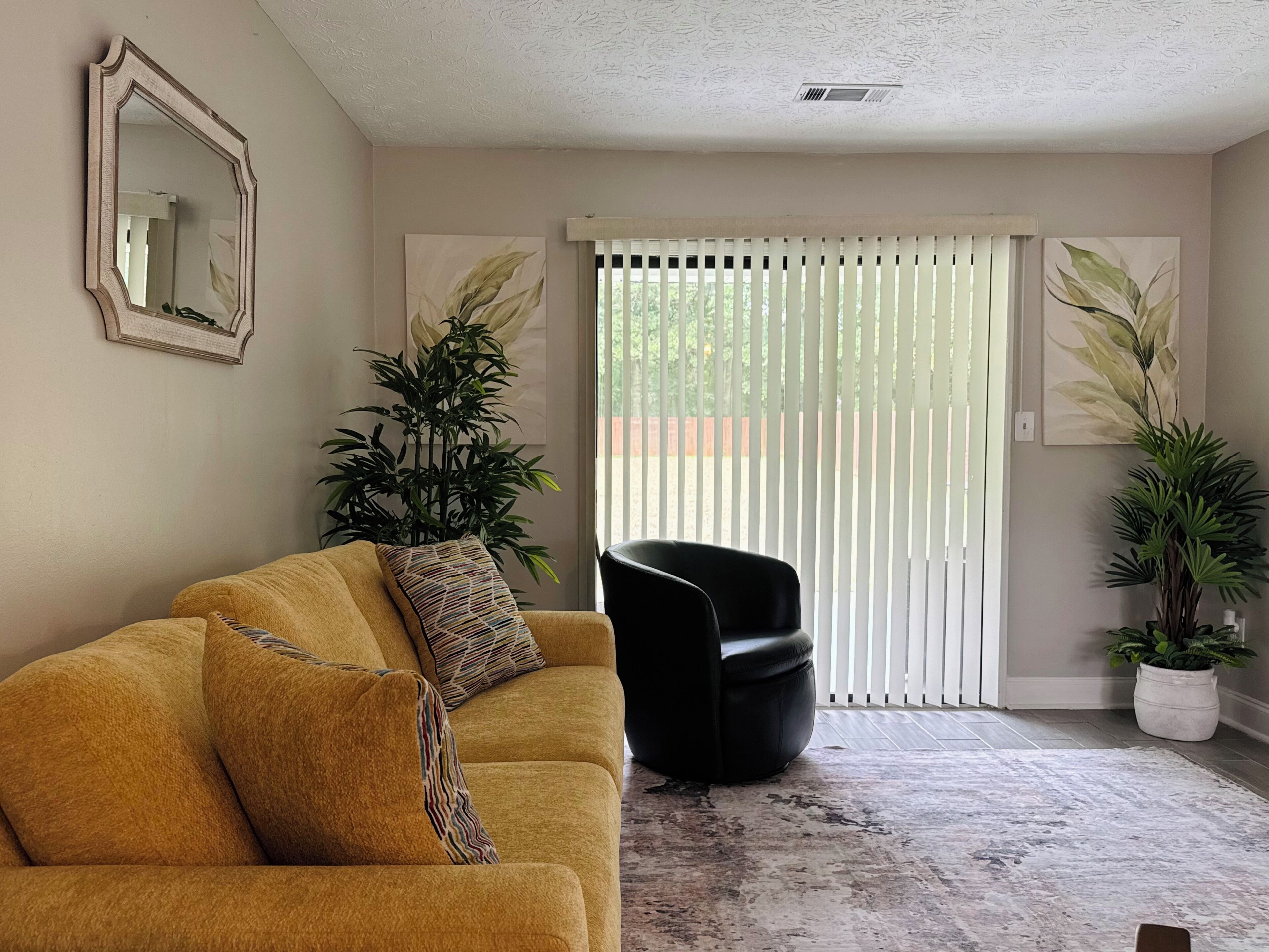 Una sala de estar con un sofá, una silla, una planta grande y un puerta corredera.