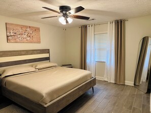 A bedroom with a bed, a ceiling fan, a window with curtains, and a painting on the wall.