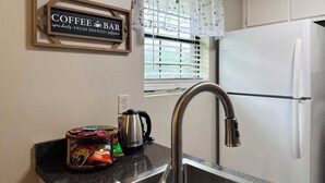Eine Küche mit einer Kaffeebar-Beschilderung, einem Fenster mit Jalousien, einem Kühlschrank und einem Spülbecken mit Wasserkocher.