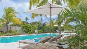 A pool area with lounge chairs and umbrellas, surrounded by palm trees and rocks. - Dolphin Suites (Willemstad)