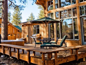 A wooden deck with outdoor furniture, a grill, and a large window overlooking a forested area. - Awesome 3000sf 4-bedroom cabin at Old Greenwood Truckee in Tahoe Mountain Club (Truckee)